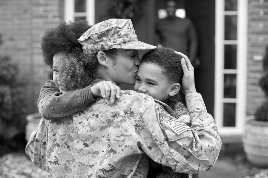 A military mom in uniform embraces her two kids in front of their home