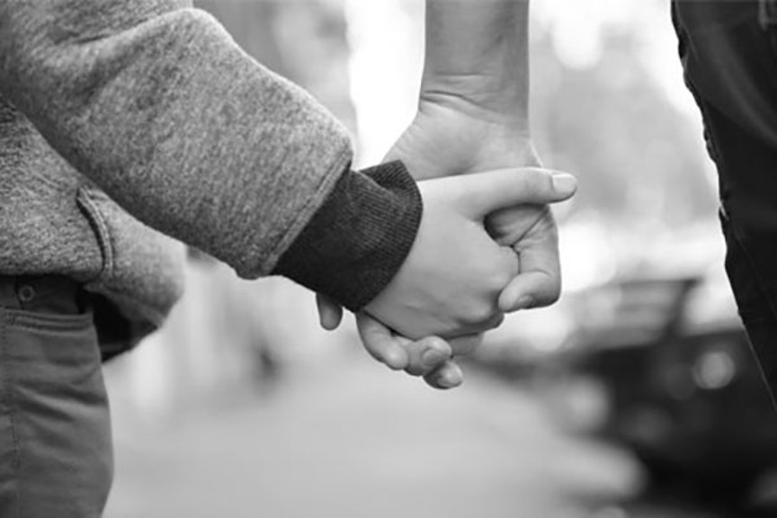 A child and adult are walking and holding hands. The child is wearing a sweater.