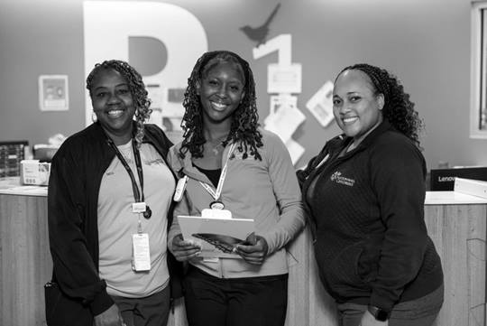 Three smiling female mentors stand in front of a nurse's station.