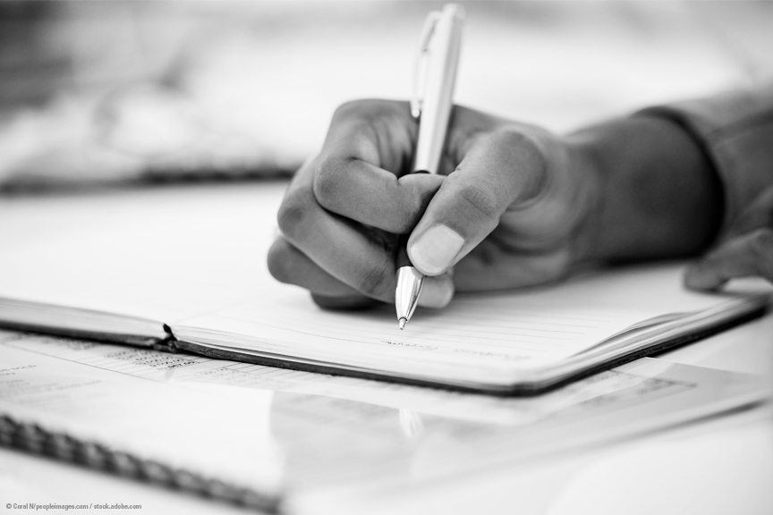A woman's hand grips a pen, writing on a piece of paper.