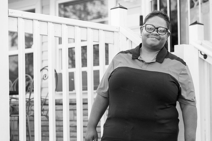 Regina is smiling, standing in front of her Linden home.