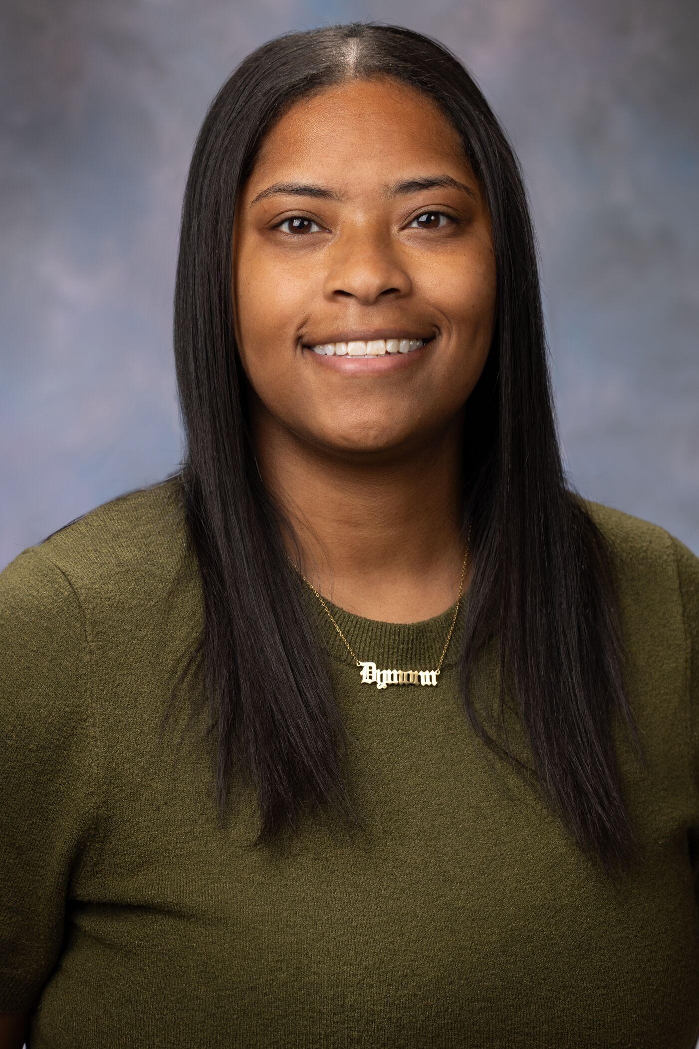 Portrait of Dymonn Johnson. Dymonn has medium length dark hair and is wearing an olive-green sweater.