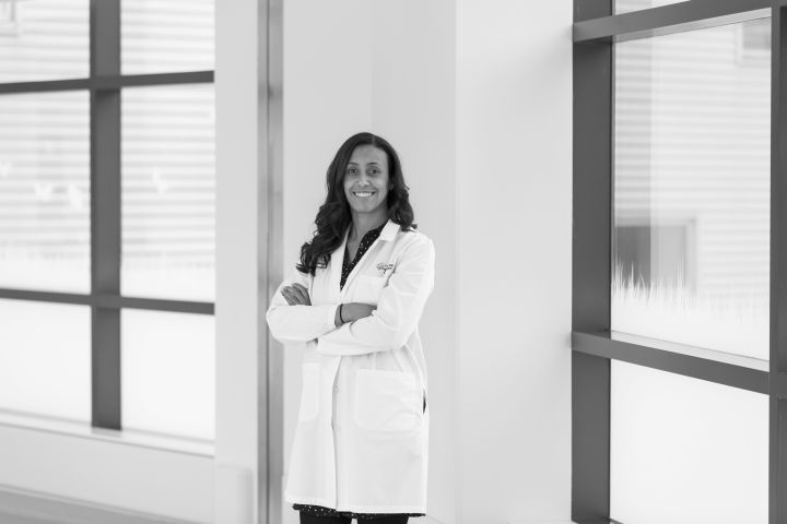 Dr. Wallihan is wearing a white coat, arms gently crossed around her body. She's smiling in a hallway with large windows behind her.
