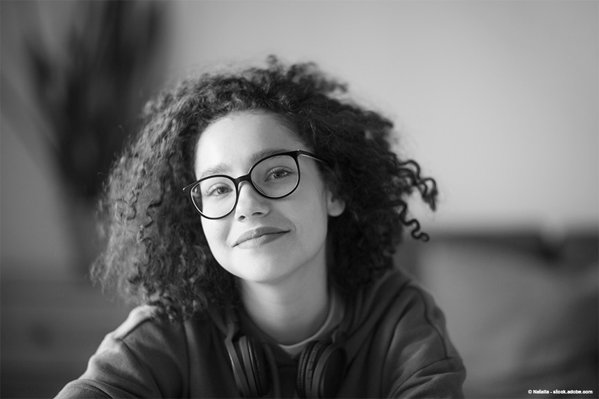 Teen girl with curly hair and dark rimmed glasses softly smiles at the camera