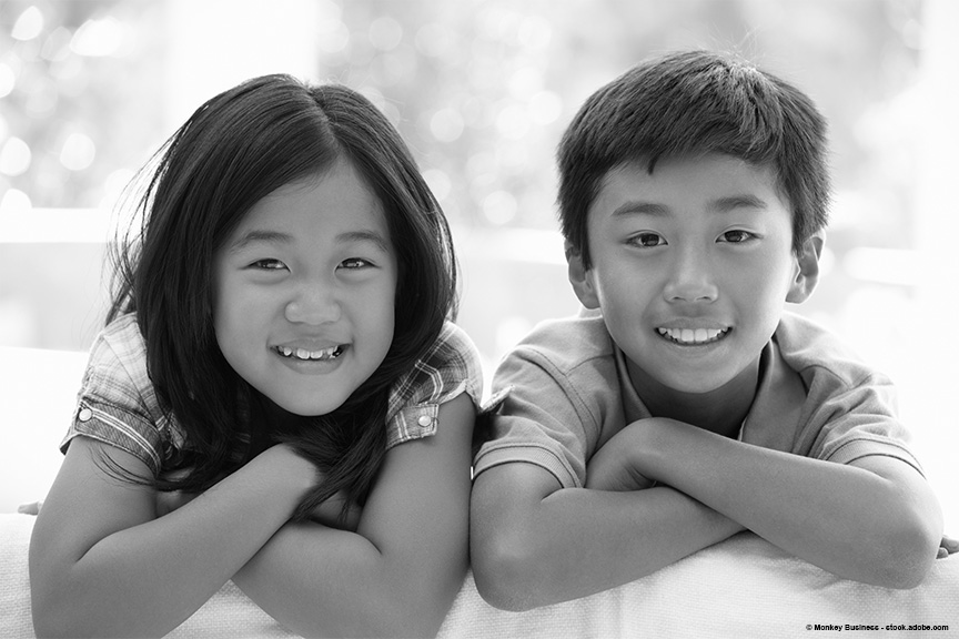 Two young children, a boy and a girl, are smiling at the camera with their arms folded in front of them.
