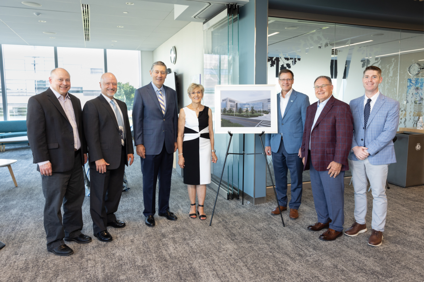 Group photo of seven smiling individuals, standing next to an easel with a large photo of a building exterior