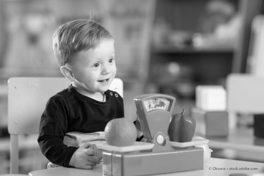 A preschool aged child is seated, smiling and playing with a toy.