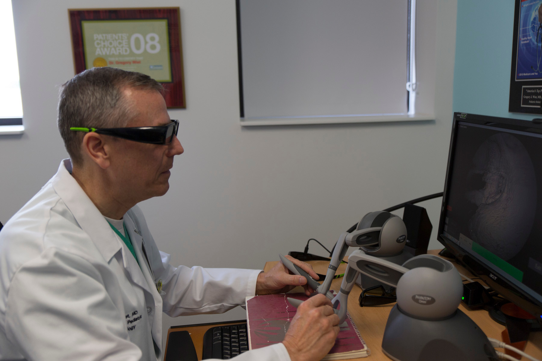 Gregory Wiet is wearing a white coat, seated at a computer with dark glasses on.