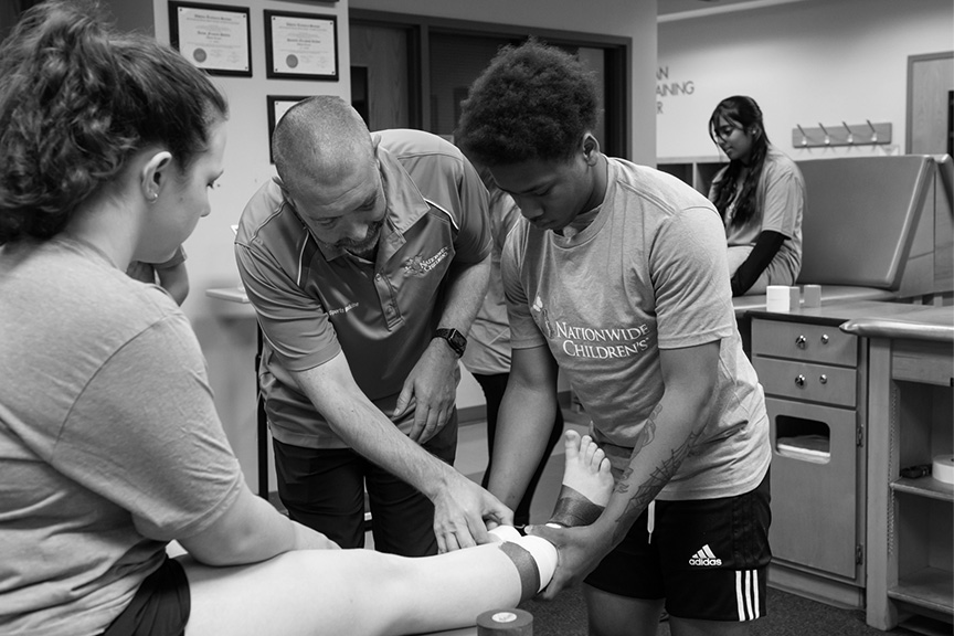 A workshop participant is wrapping a woman's ankle. The athletic trainer is watching and providing active instruction.