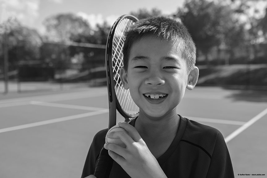 Young elementary tennis player smiling with his racket on a tennis court