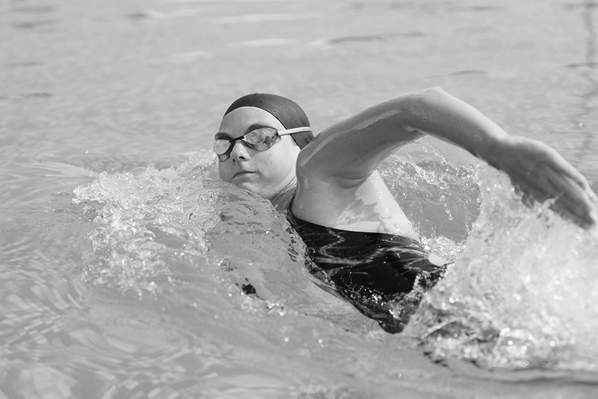Teen athlete, wearing a cap and goggles, swimming in a pool
